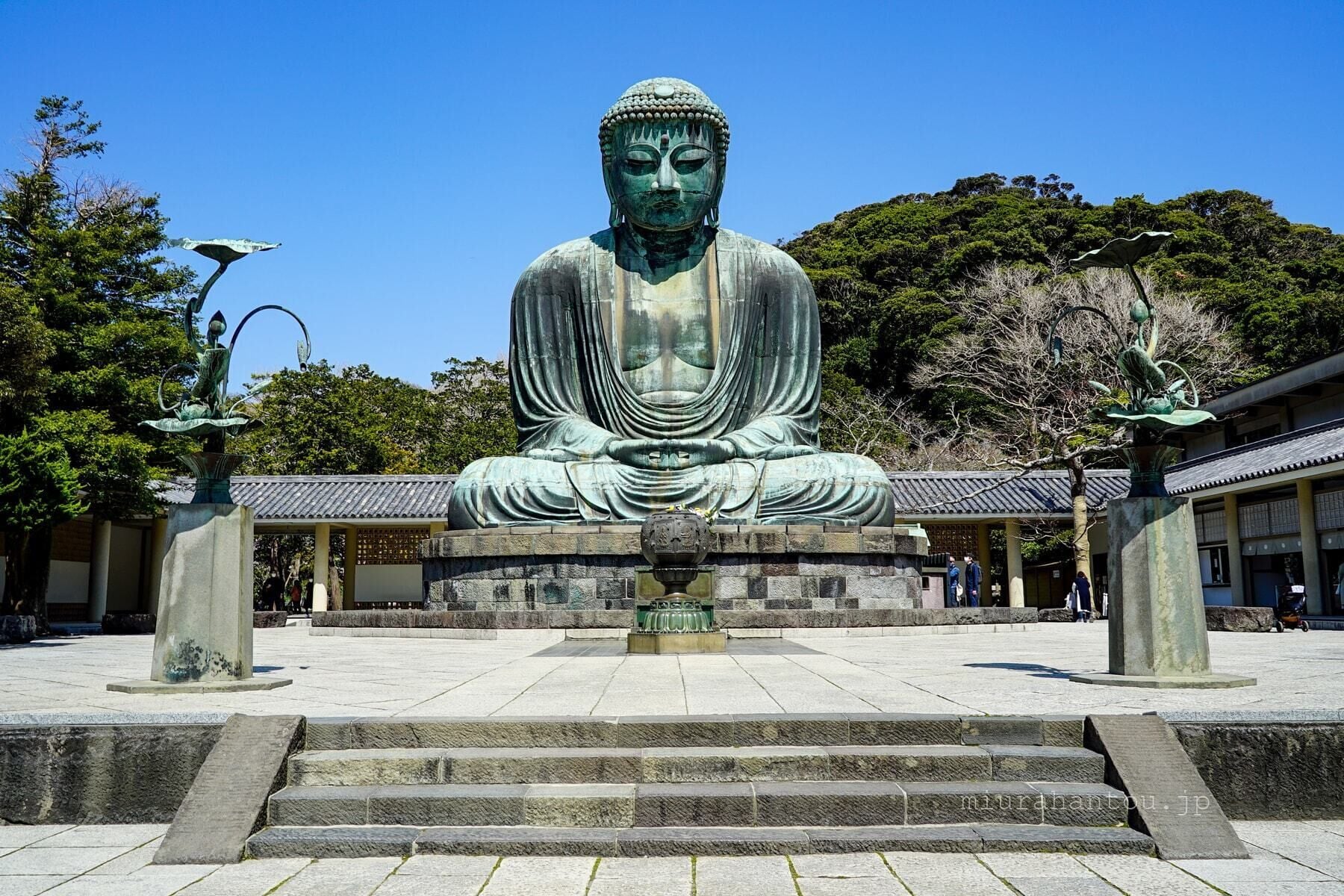 A large seated Buddha statue in a courtyard with steps leading up to it, surrounded by traditional buildings.