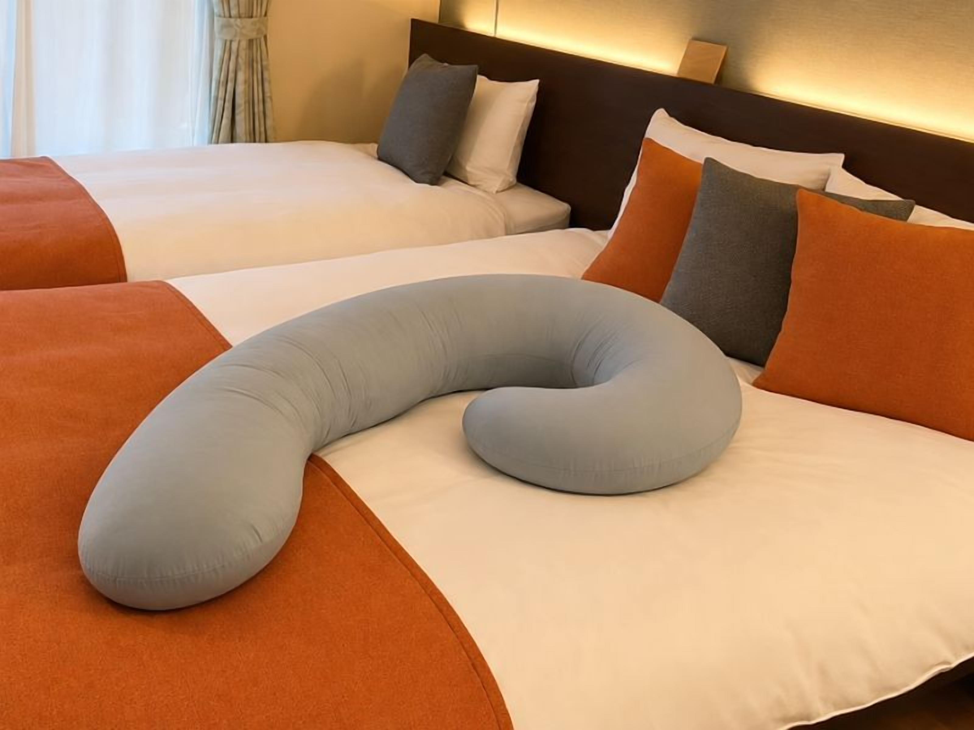 A hotel room with two beds, each with white bedding and orange accents.