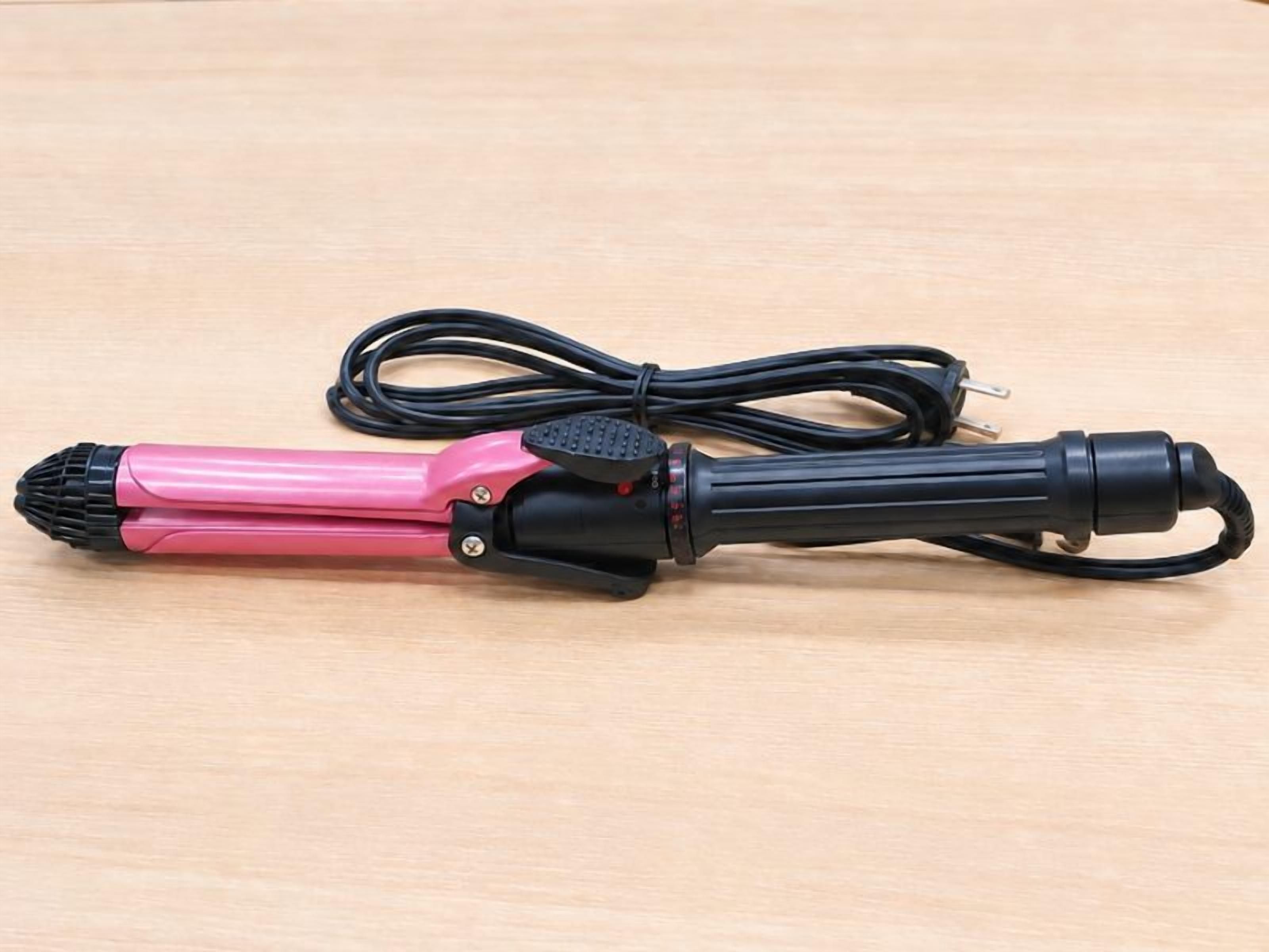 Un secador rosa y negro con cable sobre una superficie de madera.
