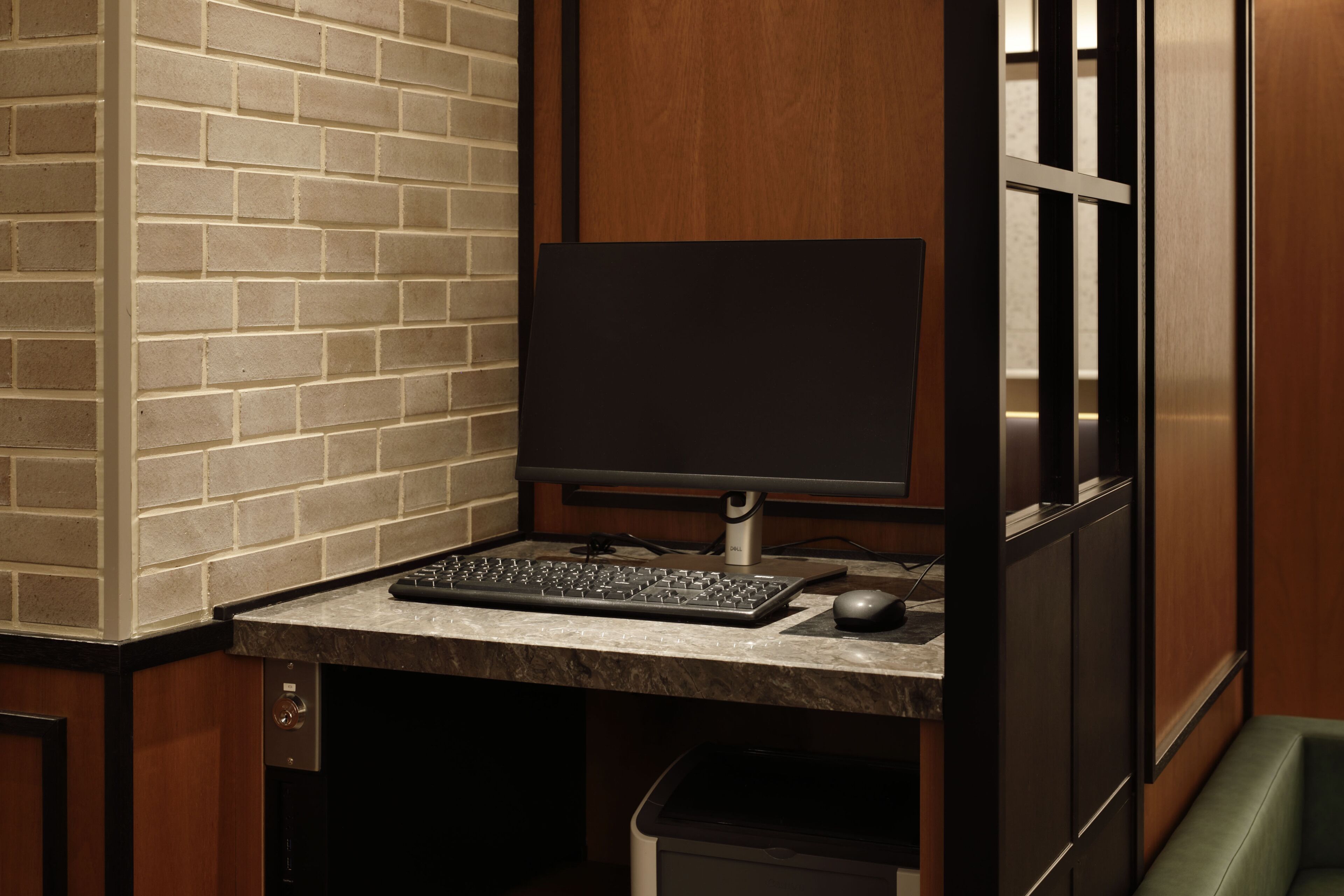 A computer desk with a keyboard, mouse, and monitor in a room with a brick wall and wooden paneling.