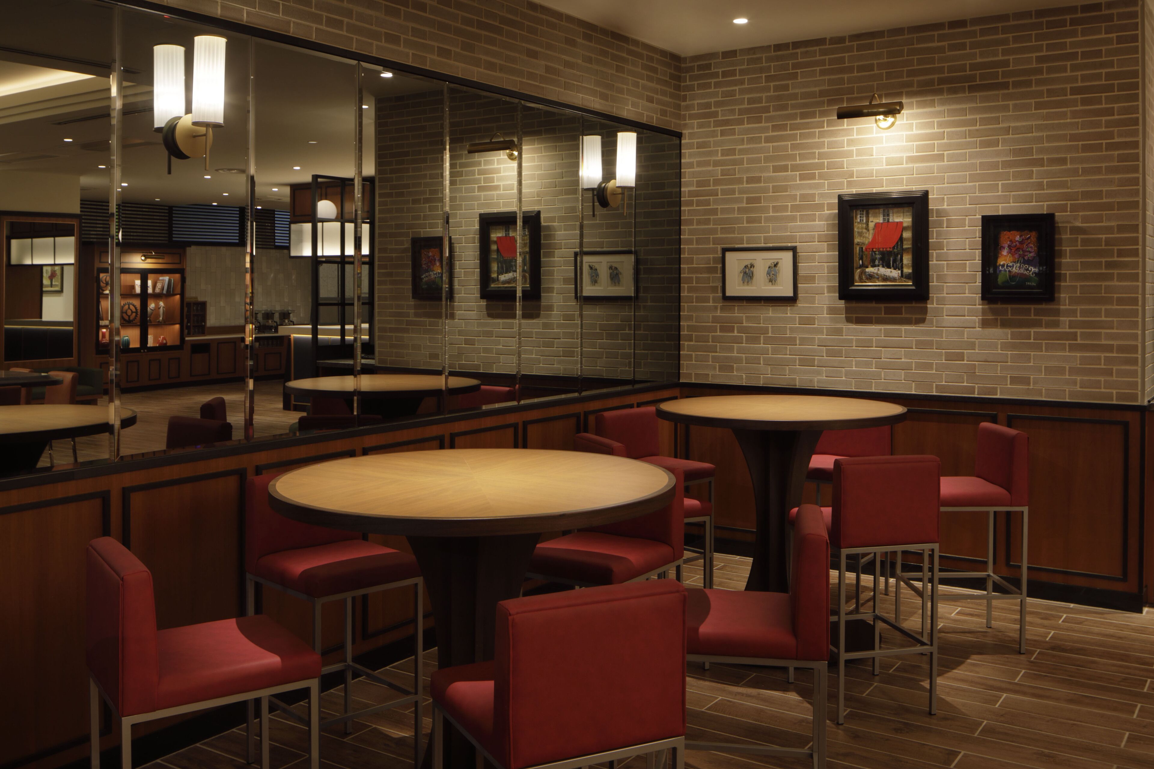 A restaurant with round tables and red chairs, brick walls, and framed pictures on the wall.