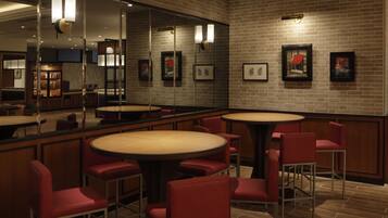 A restaurant with round tables and red chairs, brick walls, and framed pictures on the wall.