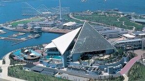 Un hotel grande y moderno con una estructura piramidal distintiva, un puerto deportivo con barcos y una vista panorámica al frente del agua.