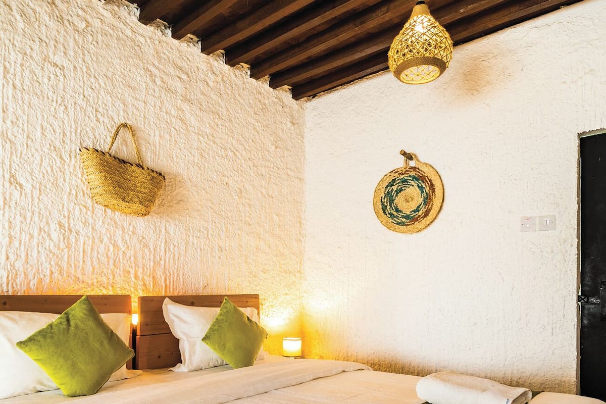 A double bed with green and white bedding, a wooden headboard, and a woven wall hanging.