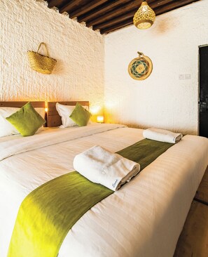 A double bed with green and white bedding, a wooden headboard, and a woven wall hanging. - SAMA Heritage Home - Al Khutaim (Al Hamra)