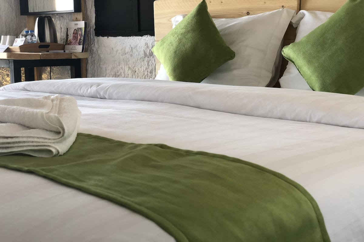 A neatly made bed with white linens, a green throw blanket, and two green pillows.