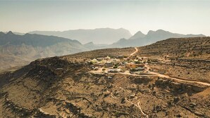 Paisatge montanyós accidentat amb un petit assentament, edificis dispersos i un camí de terra.