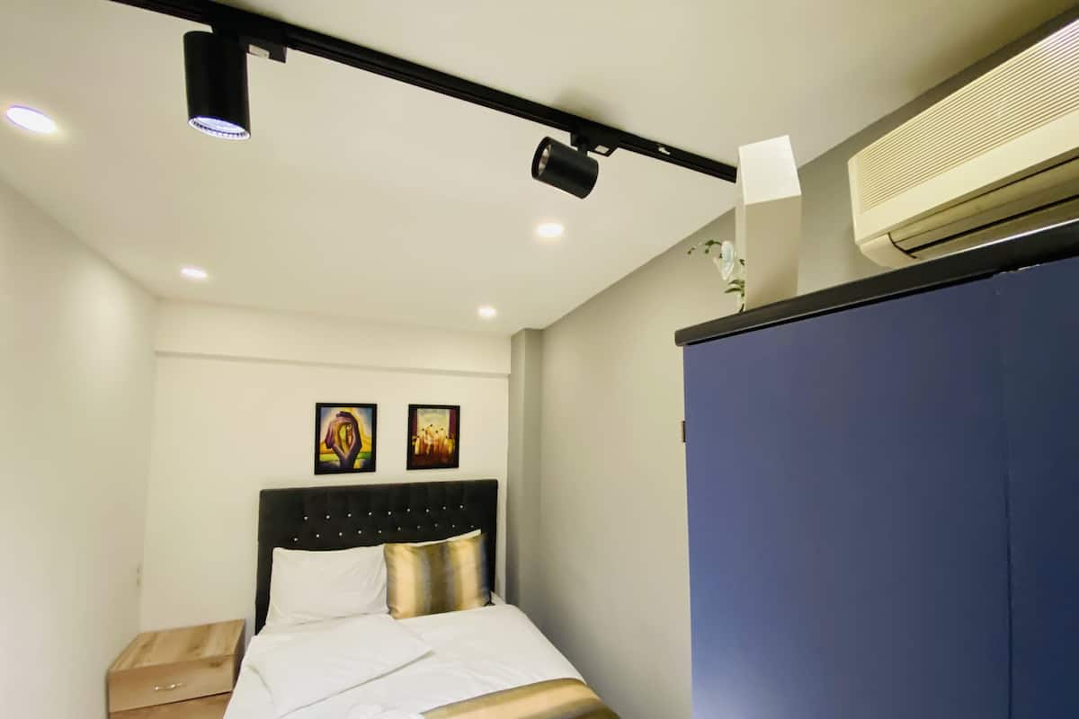 A bedroom with a bed, bedside table, wall art, and an air conditioning unit.