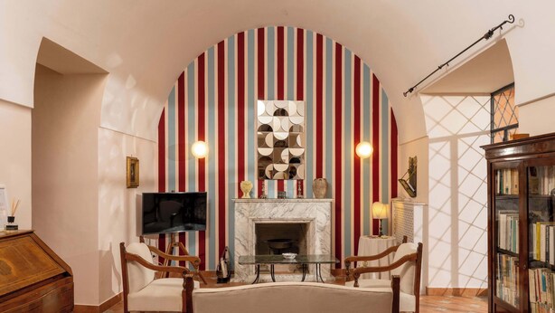 Una sala de estar con chimenea, papel tapiz a rayas, televisor y estantería.