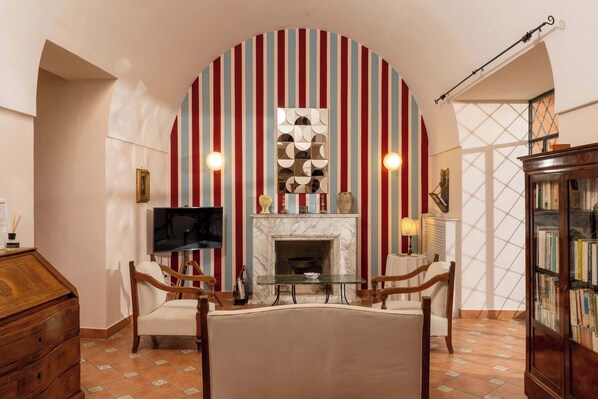 Una sala de estar con chimenea, papel tapiz a rayas, televisor y estantería.