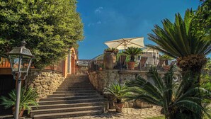 Una escalera de piedra que conduce a una terraza con asientos al aire libre y un gran paraguas.