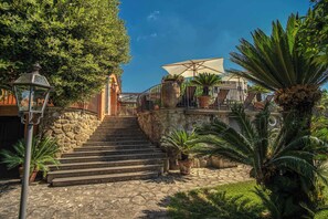 Una escalera de piedra que conduce a una terraza con asientos al aire libre y un gran paraguas.