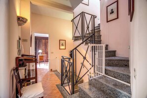 Una escalera con barandilla de metal, un banco de madera y un comedor con mesa y sillas.