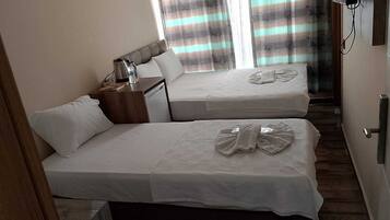 Quarto de hotel com duas camas, uma mesa de cabeceira com abajur e uma janela com cortinas listradas.
