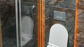 A modern bathroom with a glass shower enclosure, a toilet, and marble walls.