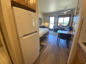 Cocina compacta con refrigerador blanco, una mesa de comedor con sillas, un sofá y una cama en la habitación contigua.