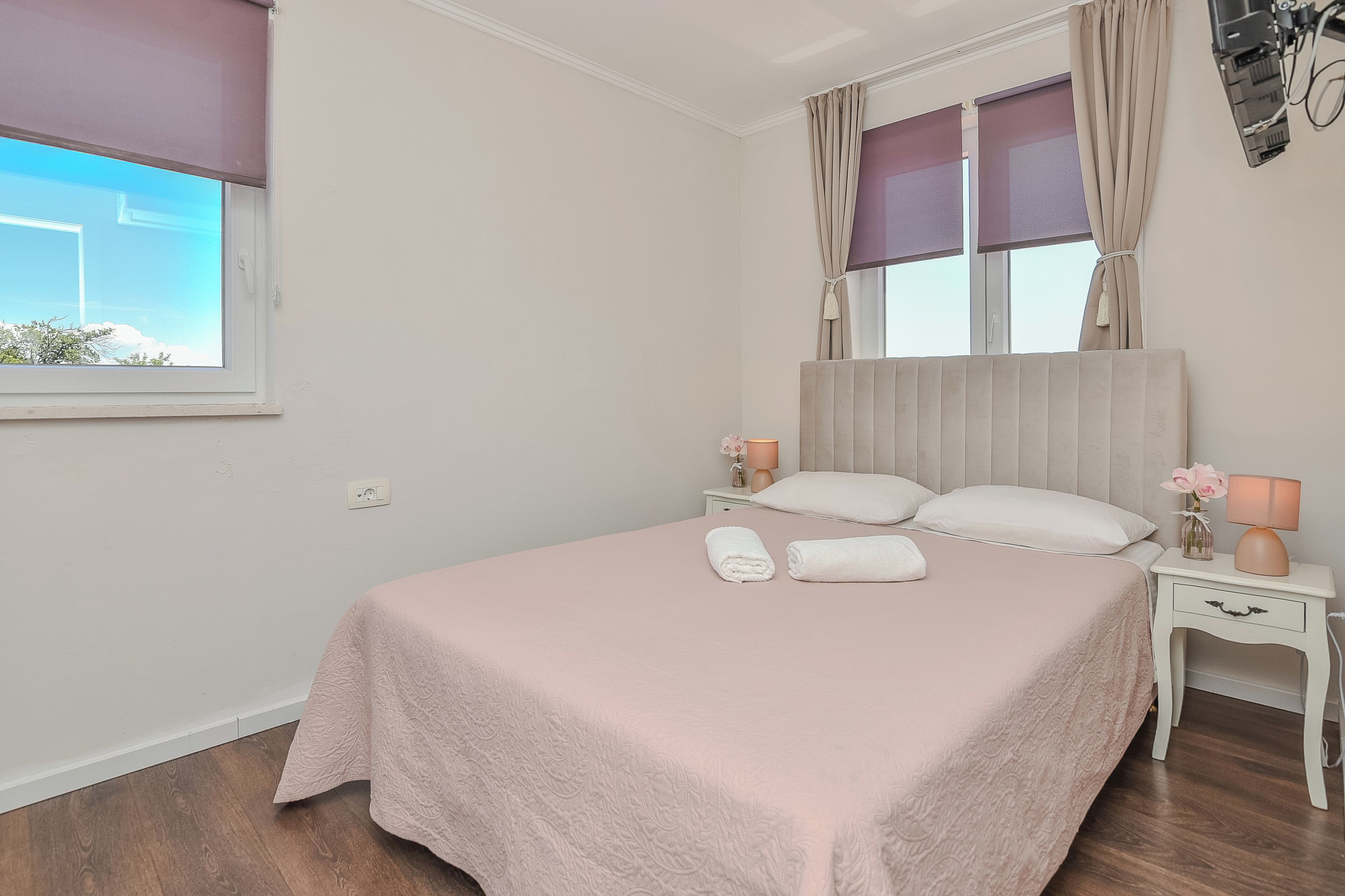 A bedroom with a bed, two bedside tables, a window with curtains, and a nightstand with a lamp.