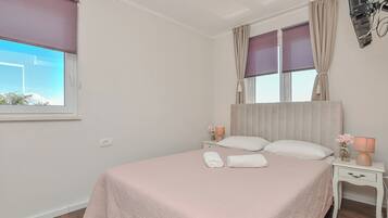 A bedroom with a bed, two bedside tables, a window with curtains, and a nightstand with a lamp.