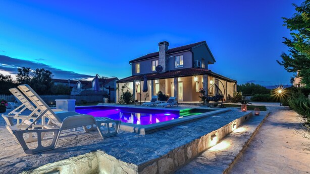Ein Haus mit Swimmingpool, Gartenmöbeln und einem gut beleuchteten Weg.