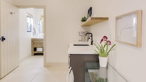 Une cuisine moderne avec des meubles blancs, un îlot central doté d’un plan de travail en verre, un évier et une orchidée en pot.