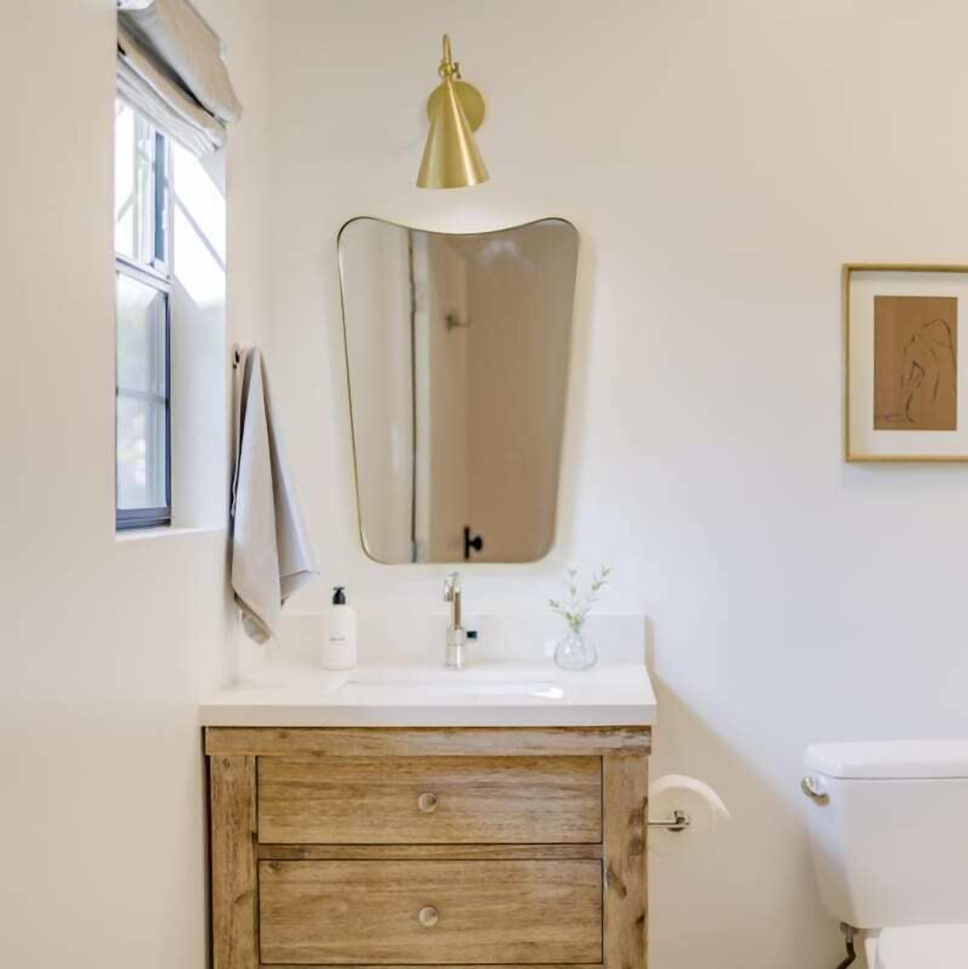 Un baño con tocador de madera, un lavabo blanco, una lámpara colgante dorada y una obra de arte enmarcada en la pared.