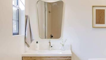 Un baño con tocador de madera, un lavabo blanco, una lámpara colgante dorada y una obra de arte enmarcada en la pared.