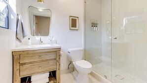 Une salle de bain avec un meuble-lavabo en bois, des toilettes blanches, une douche en verre et un tableau encadré au mur.