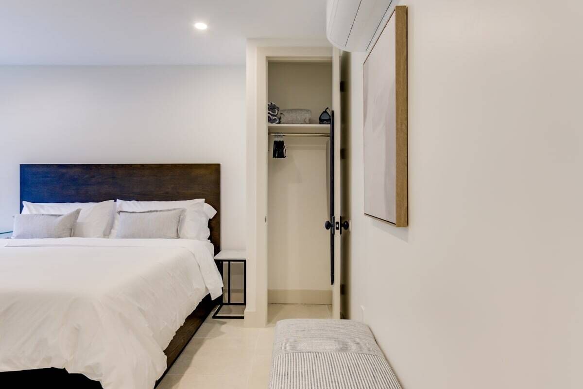 A bedroom with a bed, a bedside table, a bench, a wardrobe, and a door leading to a bathroom.
