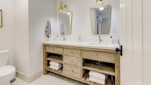 Ein Badezimmer mit einem weißen Waschbecken, zwei Spiegeln, einer Holzkommode und einer Toilette.