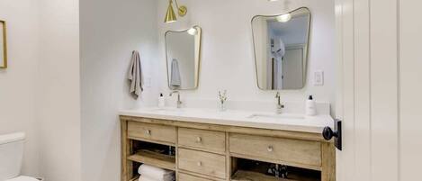 Un baño con un lavabo blanco, dos espejos, un tocador de madera y un inodoro.