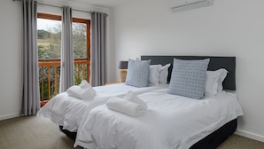 Ein Doppelbett mit weißen Leinentüchern, zwei gerollten Handtüchern, einem dunklen Kopfteil und einem Fenster mit grauen Vorhängen.
