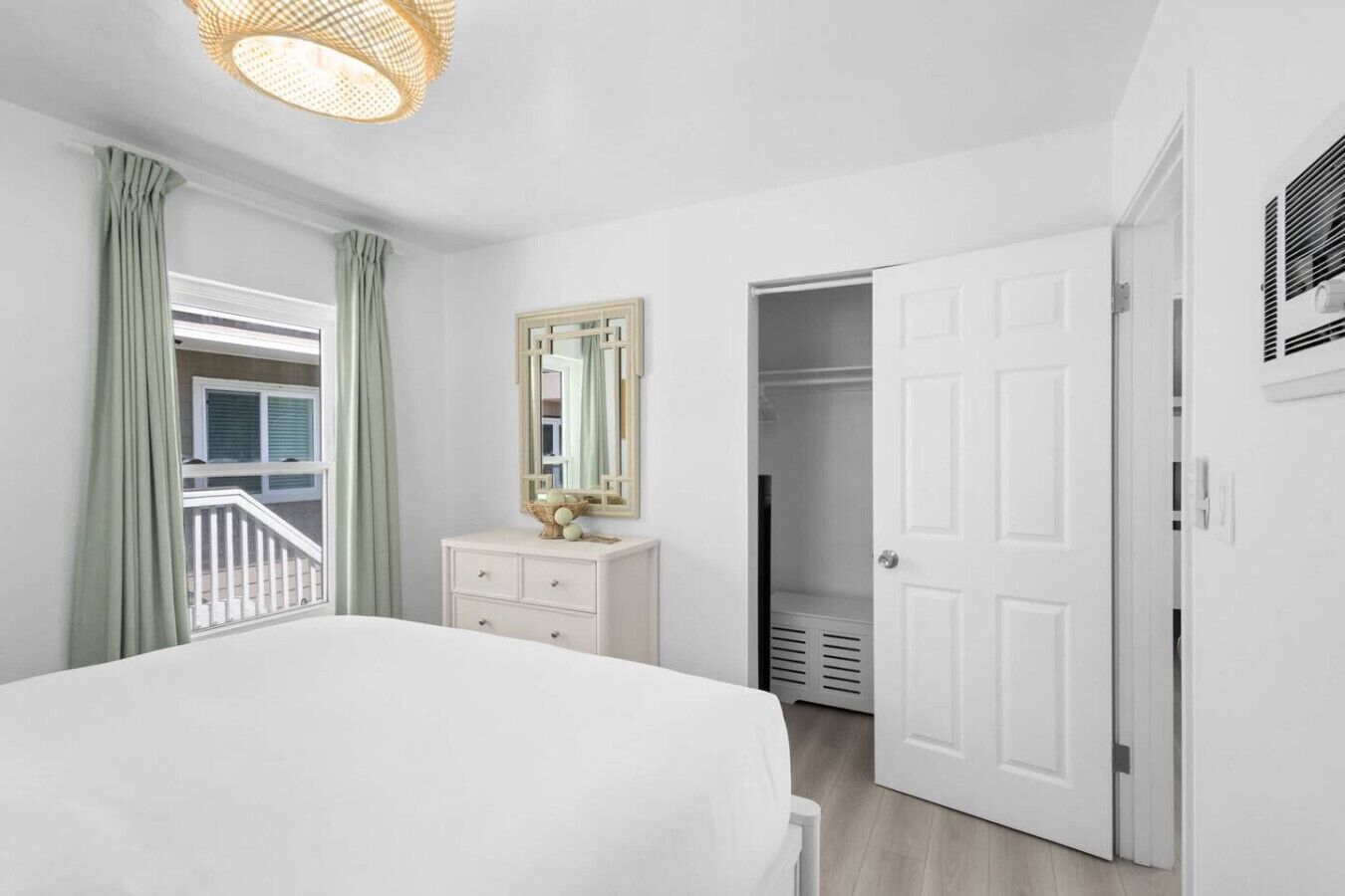 A bedroom with a bed, a dresser, a mirror, a door, and a window with curtains.