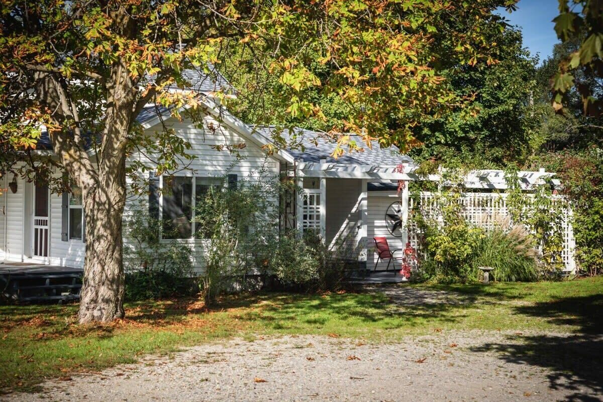 A white house with a porch, surrounded by trees and a fence.