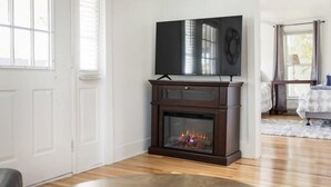 A living room with a fireplace, a television on a stand, and a round table with a book. - Ames Cottage in Elk Rapids - Dog Friendly (Elk Rapids)