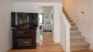 A living room with a fireplace, a television, and a staircase leading to another room. - Ames Cottage in Elk Rapids - Dog Friendly (Elk Rapids)