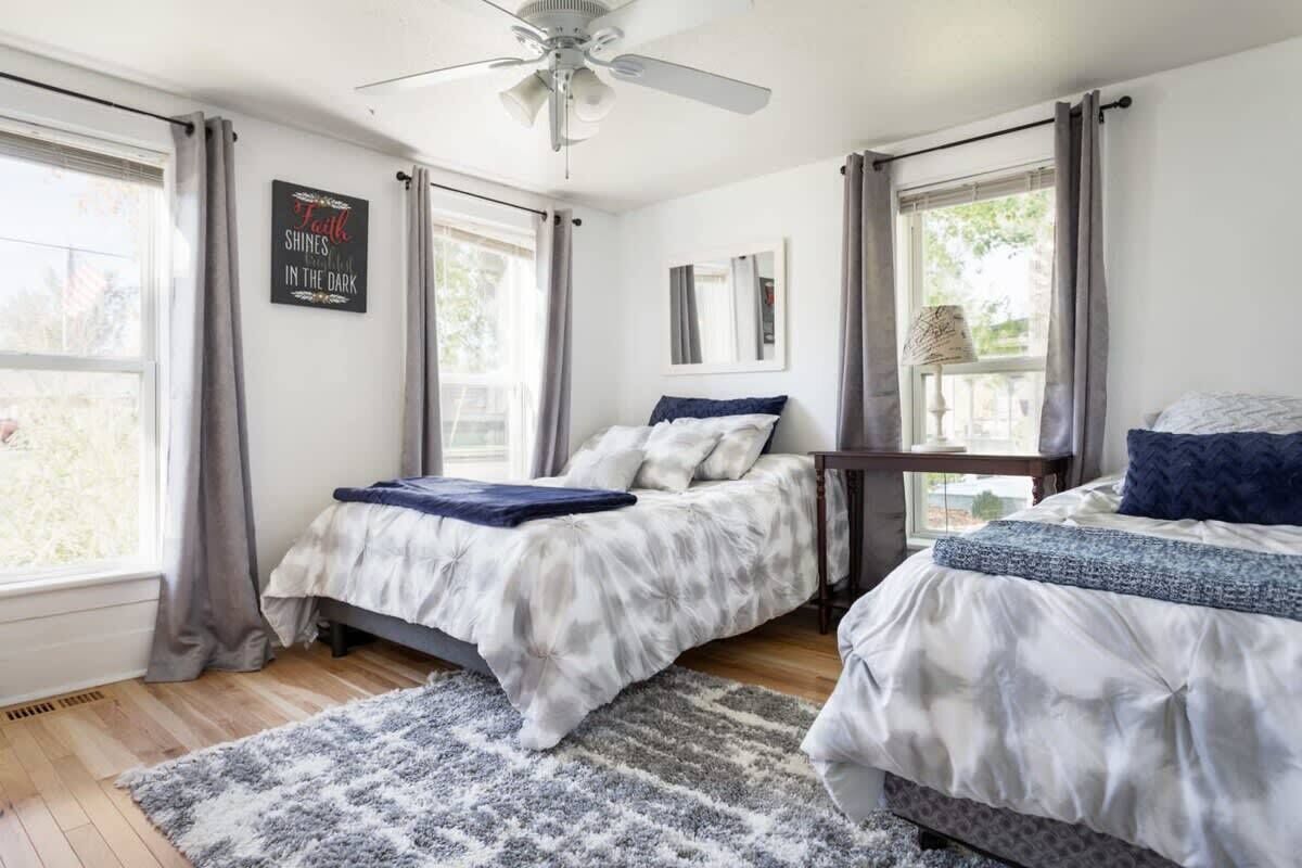 A bedroom with two beds, a ceiling fan, and a window with curtains.