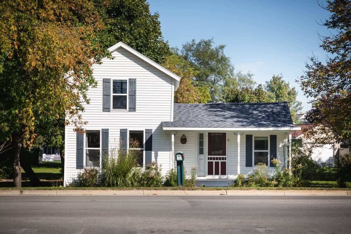 A white two-story house with a gabled roof, a front porch, and a mailbox.