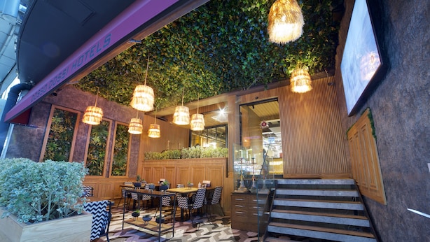 Un restaurante con una decoración moderna, que presenta una mesa y sillas de madera, luces colgantes y una escalera que lleva a un nivel superior.