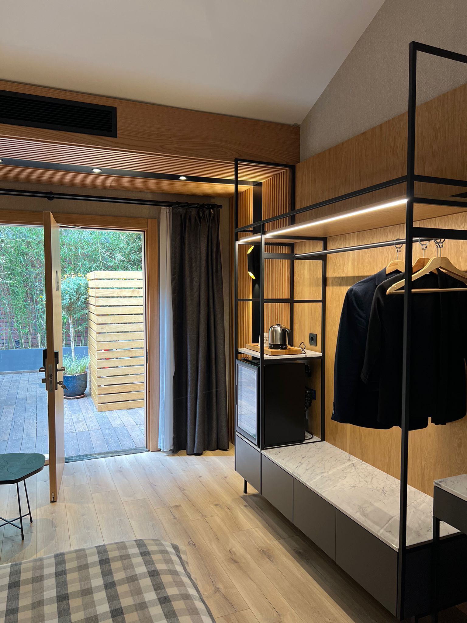 A modern bedroom with a built-in wardrobe, a small kitchenette, and a sliding glass door leading to an outdoor area.