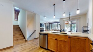 A modern kitchen with wooden cabinets, a stainless steel dishwasher, and pendant lights. - Woodwinds 1265 Luxury Townhouse, Private Hot Tub, 2 Car Garage by RedAwning (Mammoth Lakes)