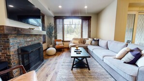 A living room with a fireplace, a sofa, a coffee table, and a TV. - Woodwinds 1265 Luxury Townhouse, Private Hot Tub, 2 Car Garage by RedAwning (Mammoth Lakes)