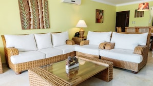 A living room with two wicker sofas, a glass coffee table, and a wall-mounted air conditioner. - Private Beach Club & Amazing Golf- Yours to enjoy, with unlimited free golf. (Punta Cana)