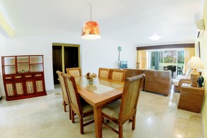 Een eethoek met een houten tafel en stoelen, een tafel met glazen blad, en een decoratieve hanglamp.