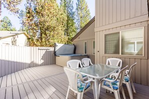 A deck with a glass table and white chairs, a hot tub, and a wooden fence.