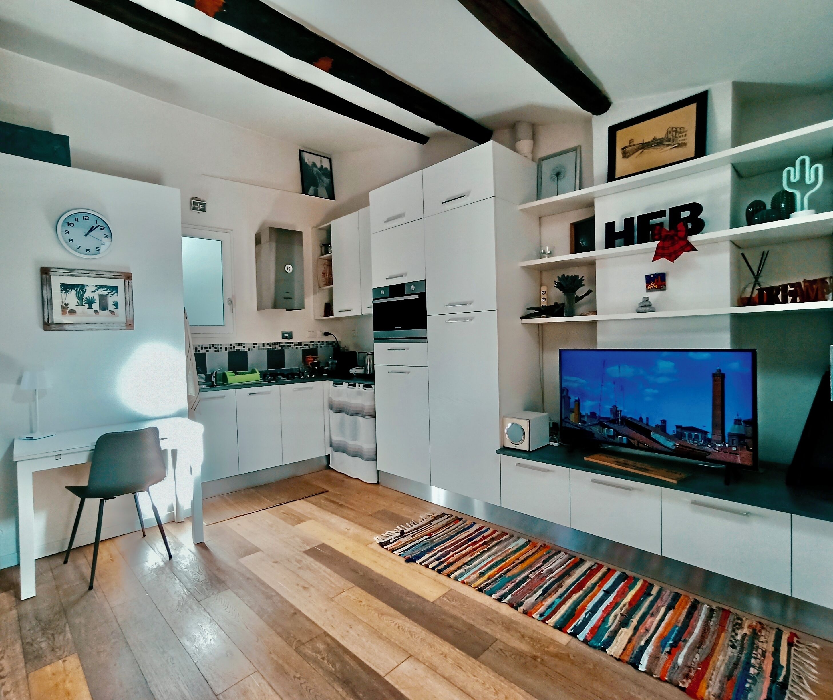 Una cucina moderna con mobili bianchi, forno a incasso e televisore su supporto.
