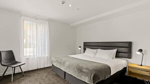 Une chambre d’hôtel moderne avec un grand lit, une chaise, une table de chevet et une fenêtre avec des rideaux.