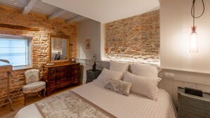 Un dormitorio con pared de piedra, cómoda de madera, cama con ropa blanca y lámpara colgante.