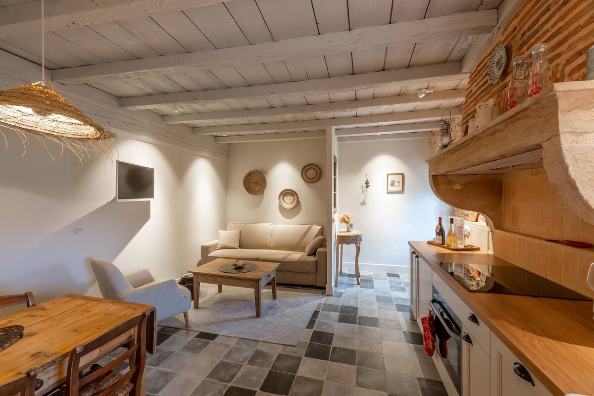 Un salon chaleureux avec un canapé, une table basse et une table à manger. On aperçoit également une cuisine avec un comptoir et des placards.