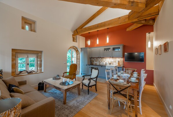 Un espacio habitable amplio con techo de madera, una mesa de comedor dispuesta para una comida y una cocina con armarios azules y un televisor.