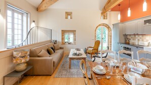 Un salón amplio con escalera de madera, una mesa de comedor preparada para seis personas y una cocina con armarios blancos y una pared de acento roja.